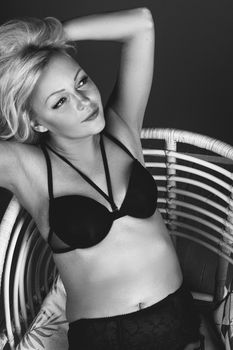 Stylish monochrome portrait of a woman in lingerie on a rattan chair.