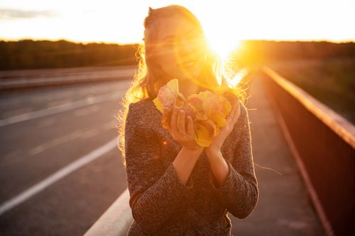 Free A woman holds autumn leaves in the golden glow of sunset on a bridge, capturing the essence of fall. Stock Photo