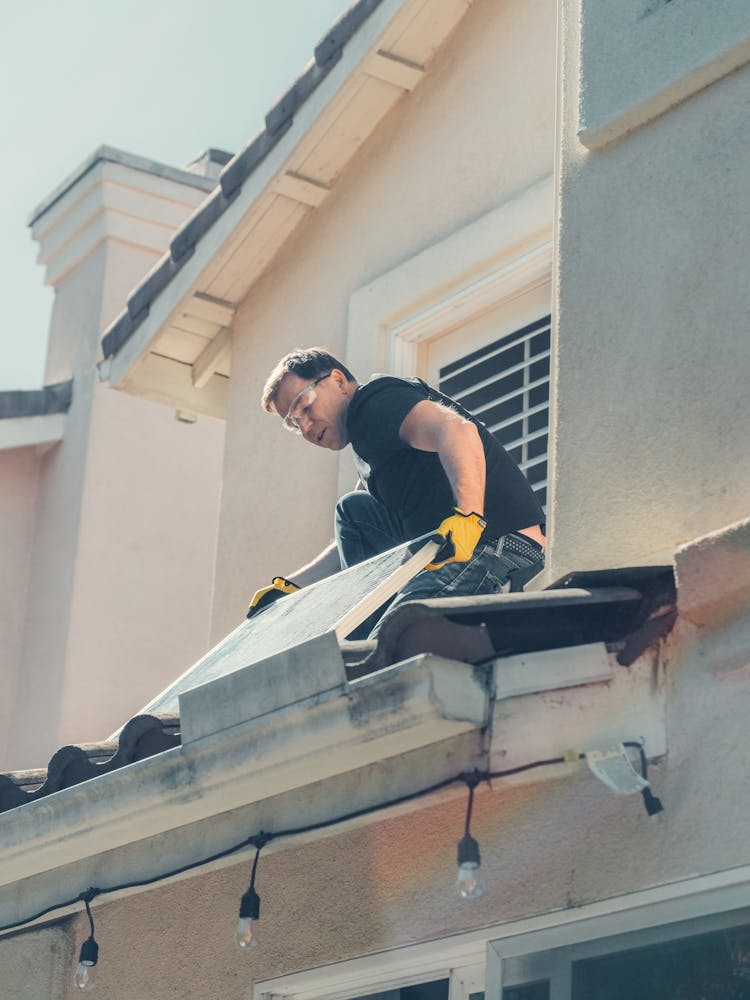 A Low Angle Shot Of A Man In Black Shirt Installing A Solar Panel On The Roof