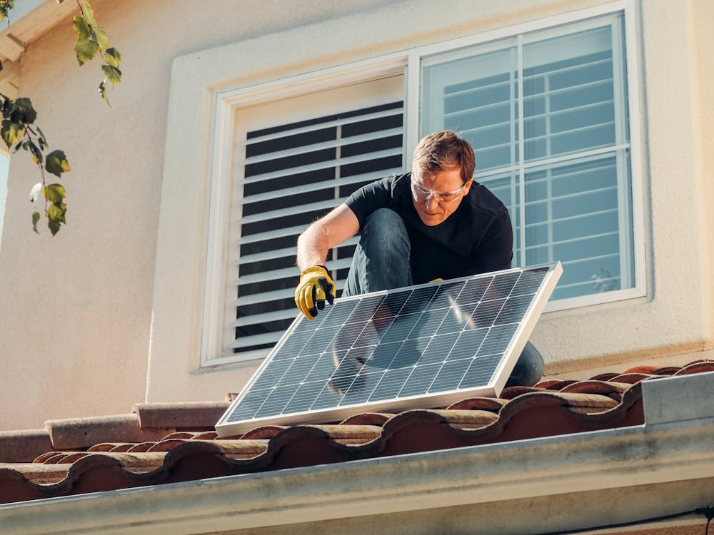 Free Man with Gloves Holding Solar Panels on the Roof Stock Photo