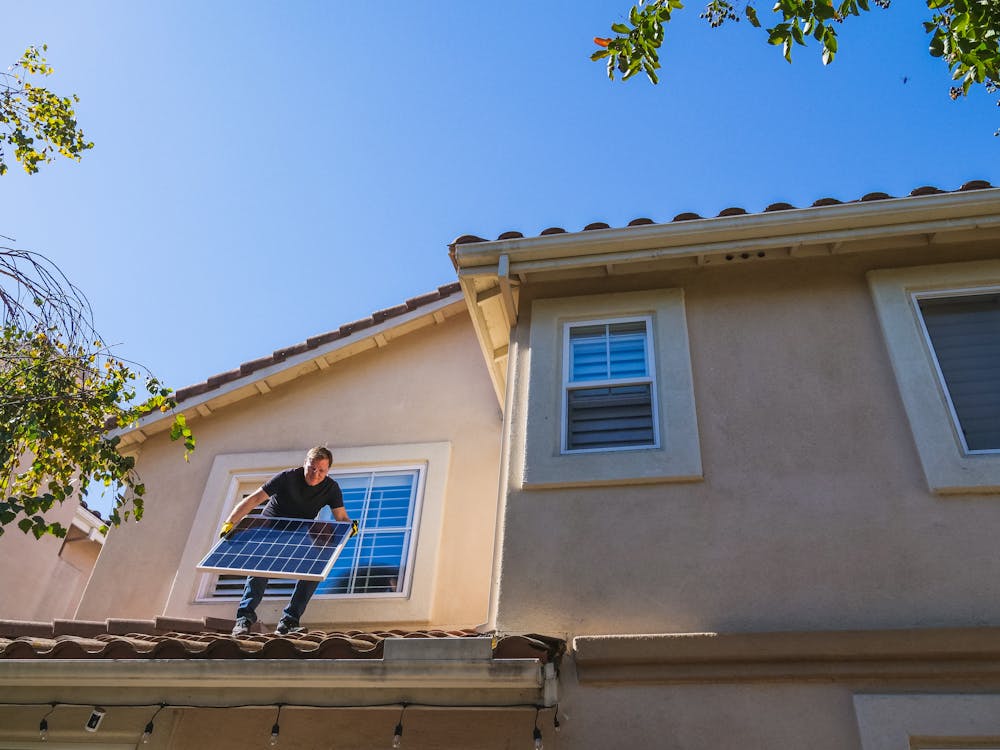 Free A Man Standing on the Roof while Holding a Solar Panel Stock Photo