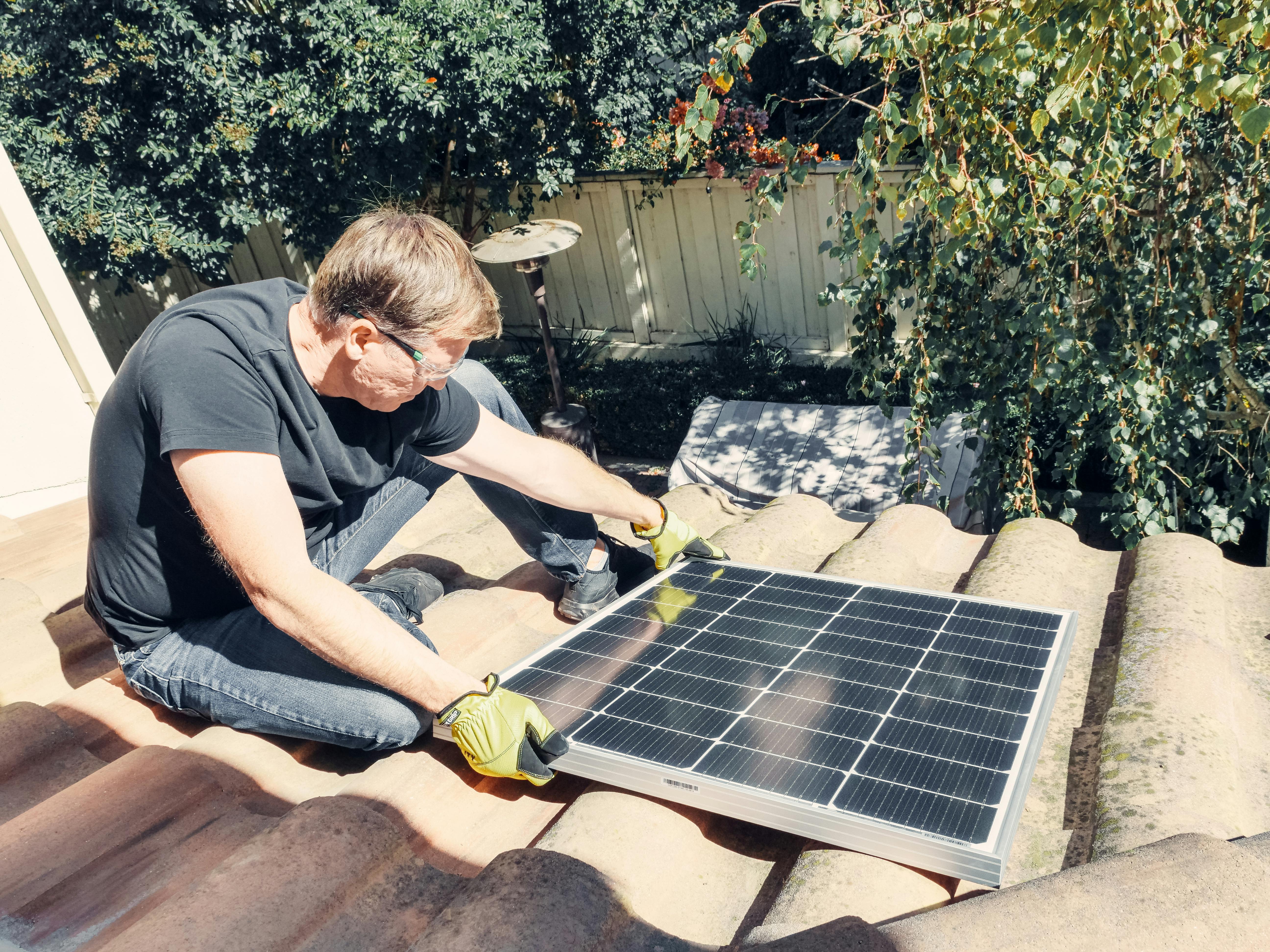 a man in black shirt sitting on the roof while holding a solar panel