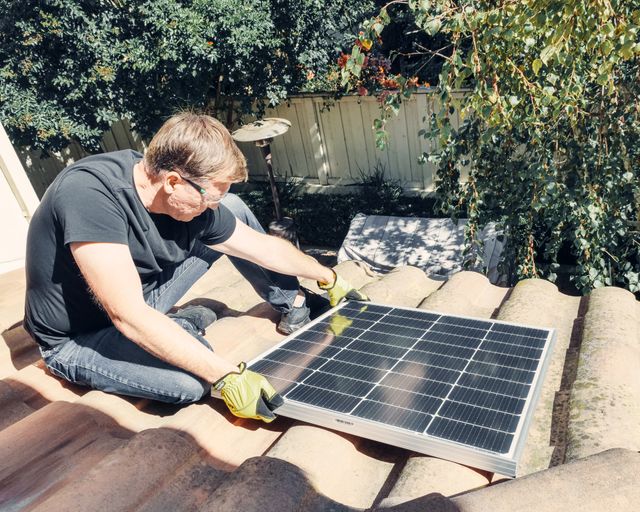 Solar panel work on a roof Technician sitting on a roof holding a solar panel during install