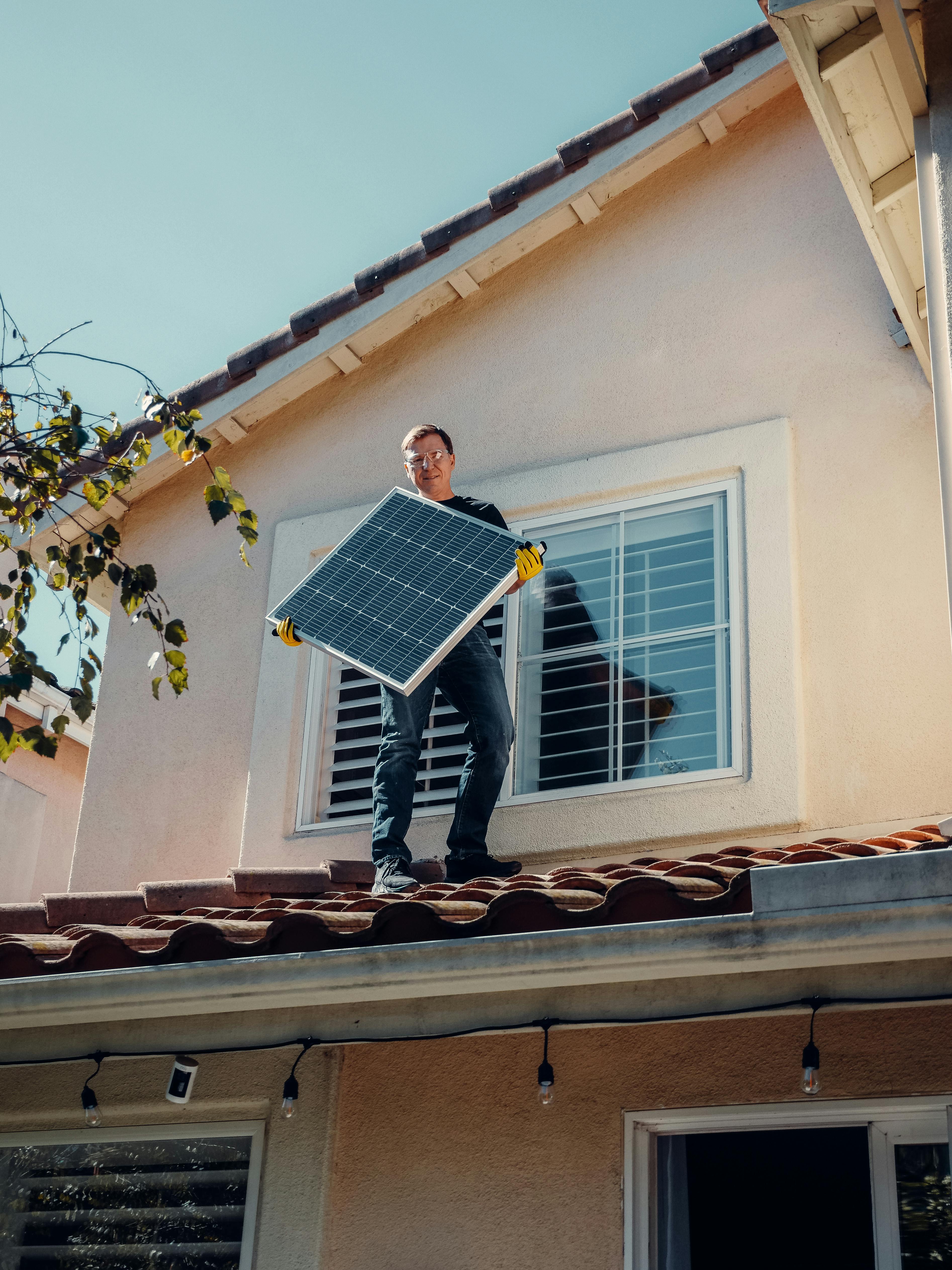 An adult male worker installing a solar panel on a house roof, showcasing clean energy in action.