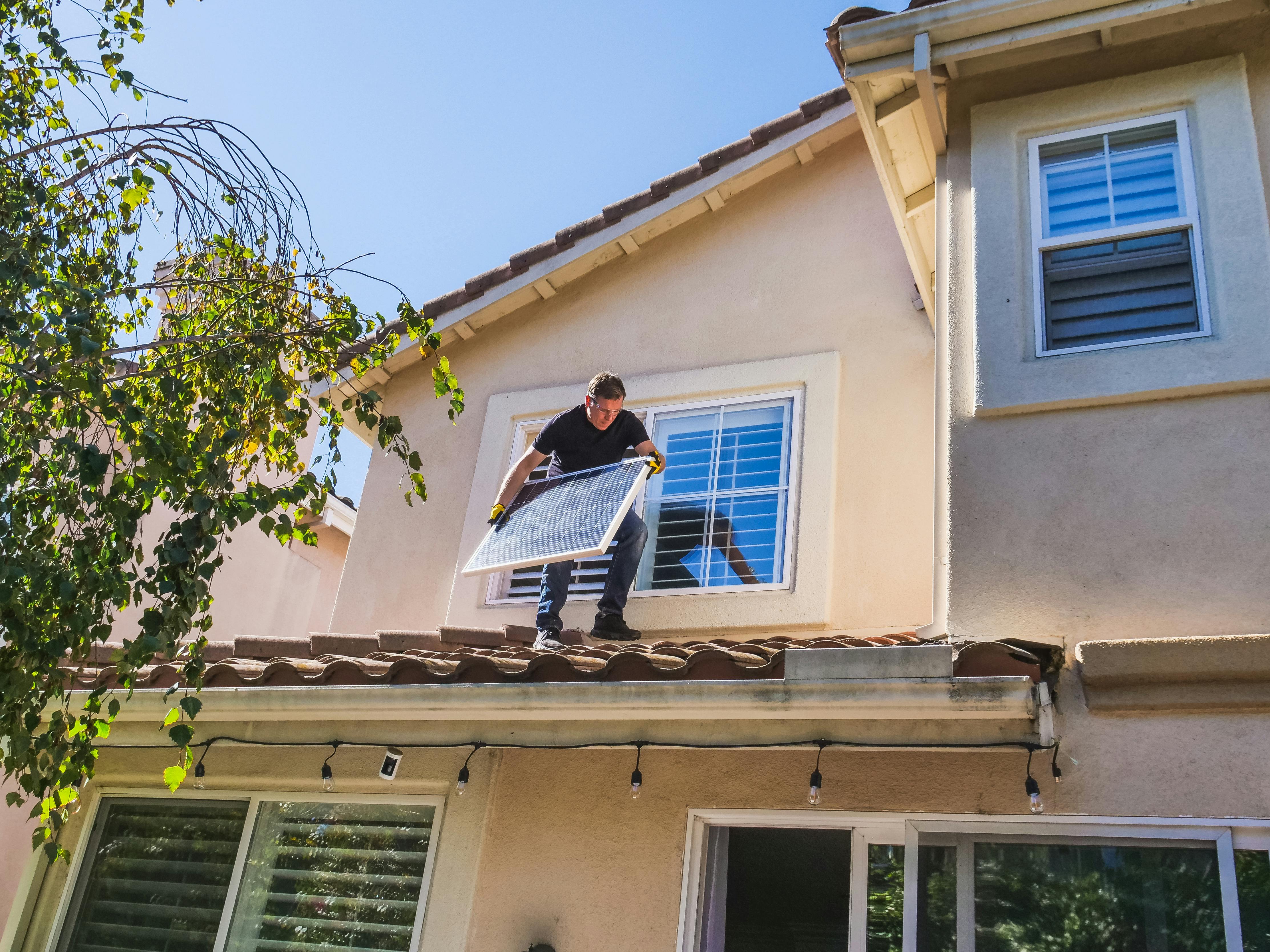 a man standing on the roof holding a solar panel