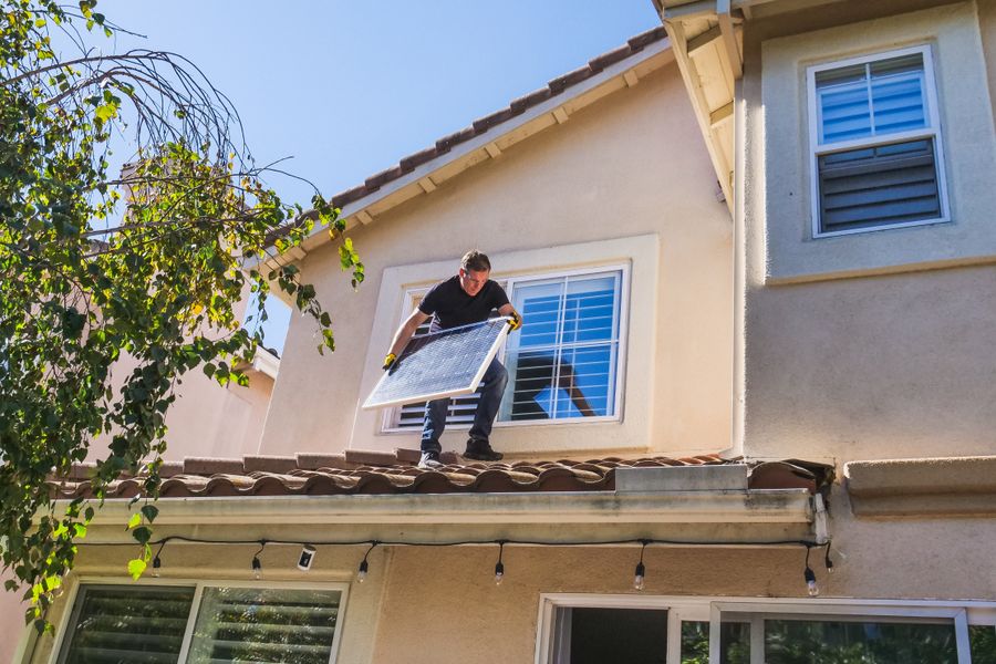 A solar technician installing panels on a house roof, emphasizing renewable energy.