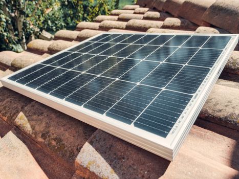 Close-up of a solar panel installed on rooftop tiles under bright daylight, emphasizing renewable energy.