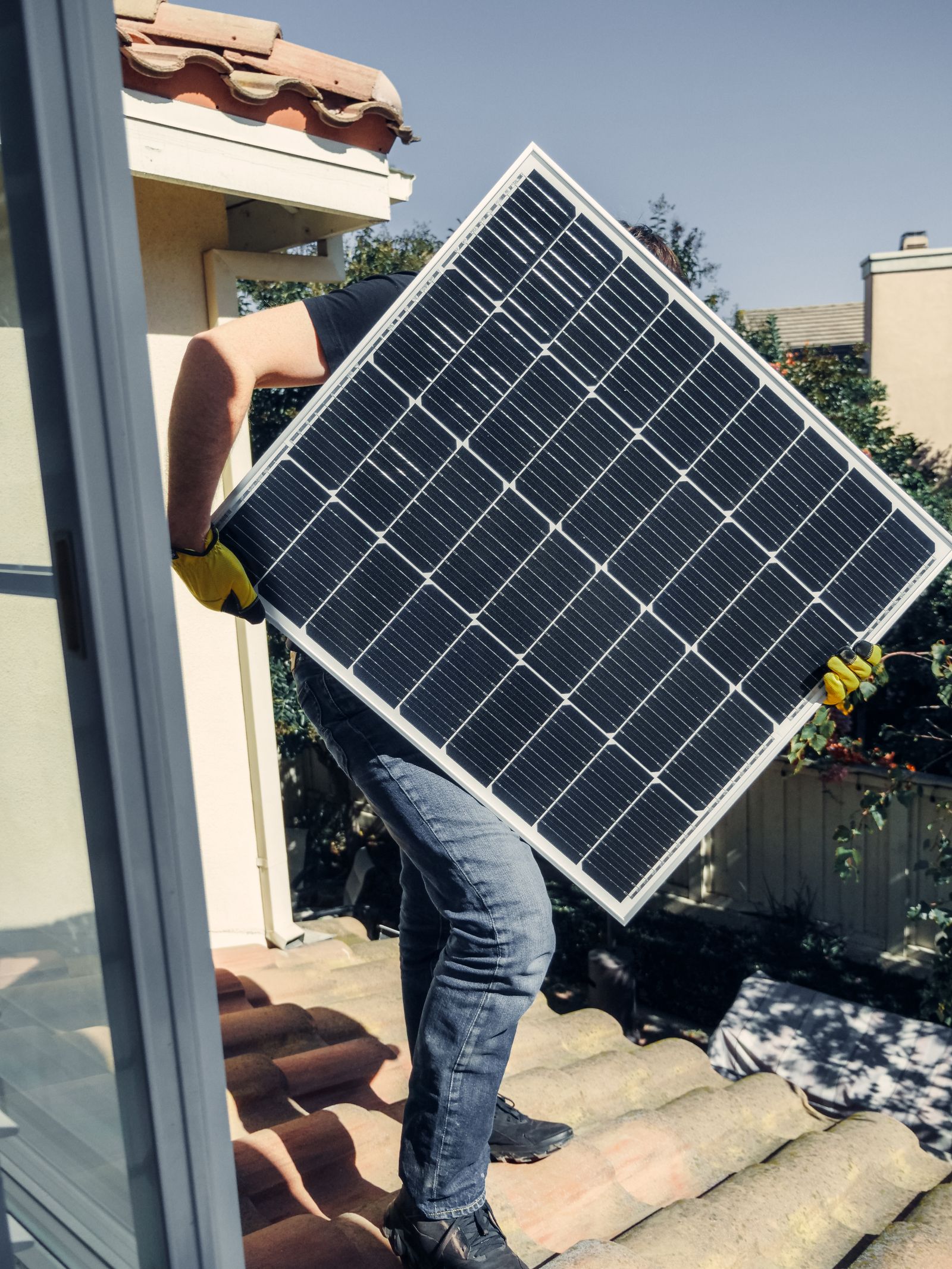 Installer carrying a solar panel across a roof