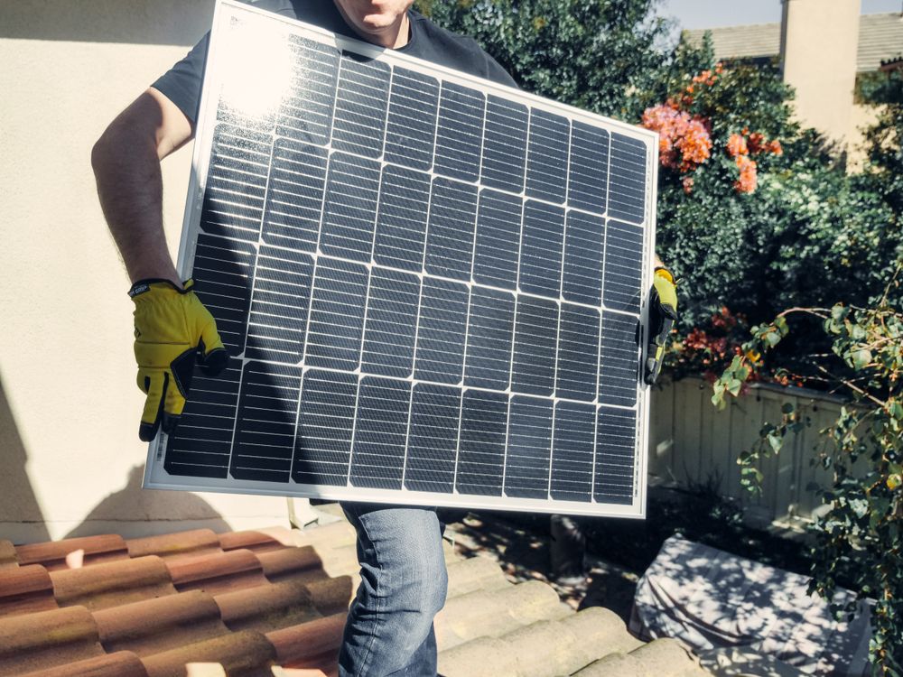 Technician carrying a solar panel on a rooftop