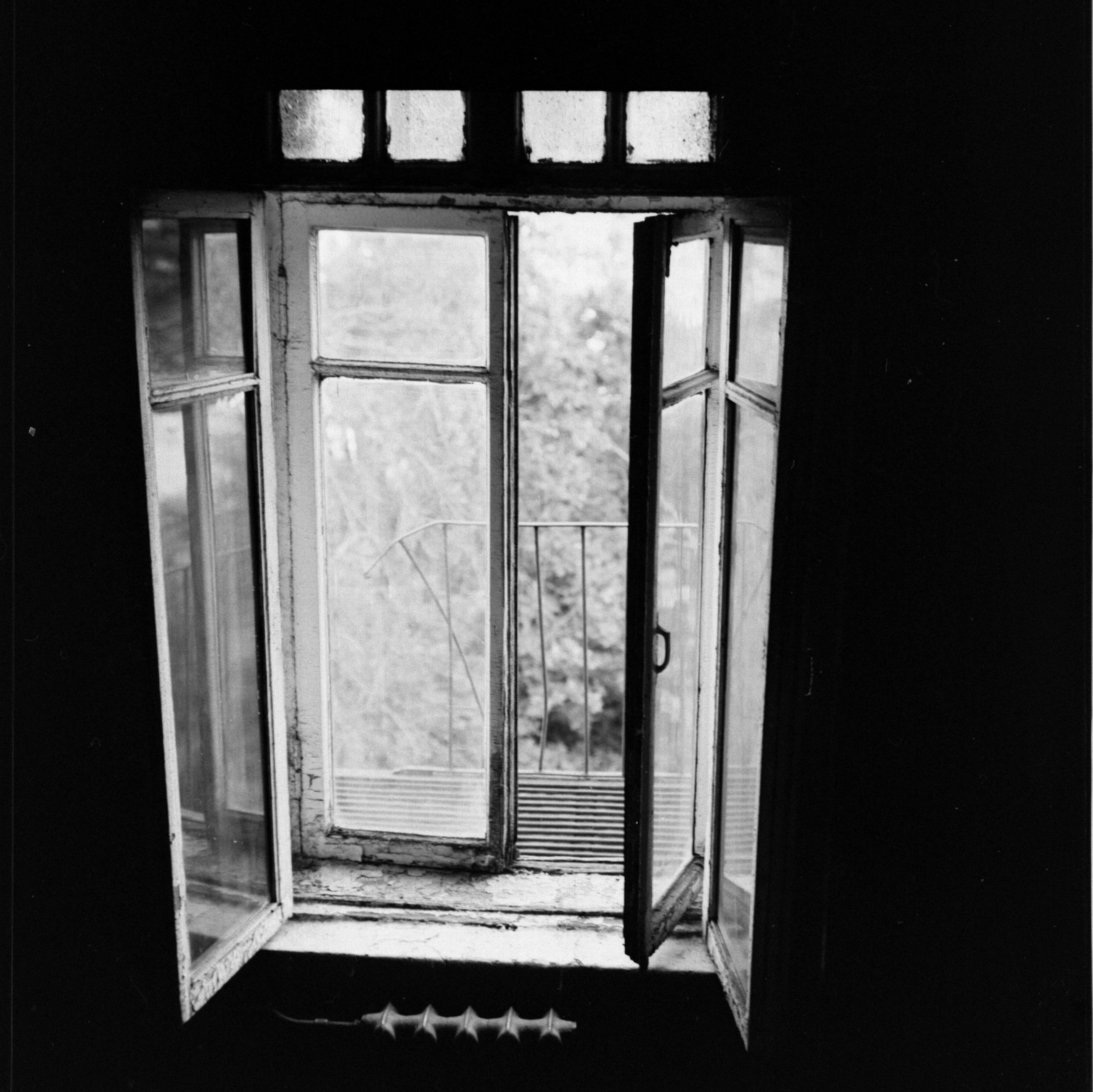 A moody black and white photograph of an open window with an outer view.