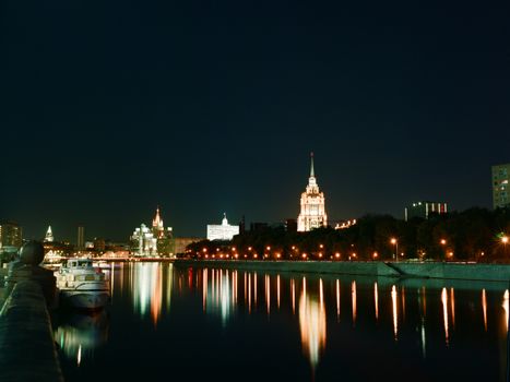 Cityscape at night with illuminated buildings and reflections on the river, creating a scenic view.