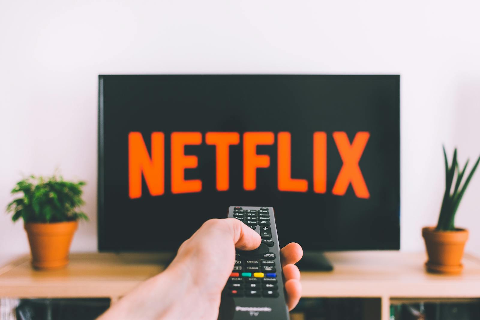 Persona che punta un telecomando verso la TV con interfaccia Netflix visibile