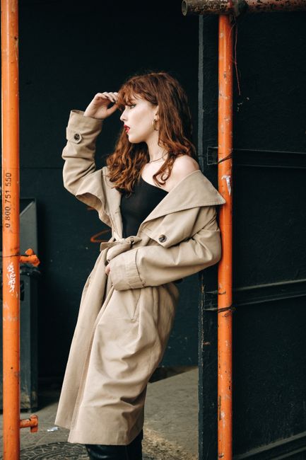 Stylish woman in a trench coat poses against an industrial backdrop, exuding modern fashion vibes.