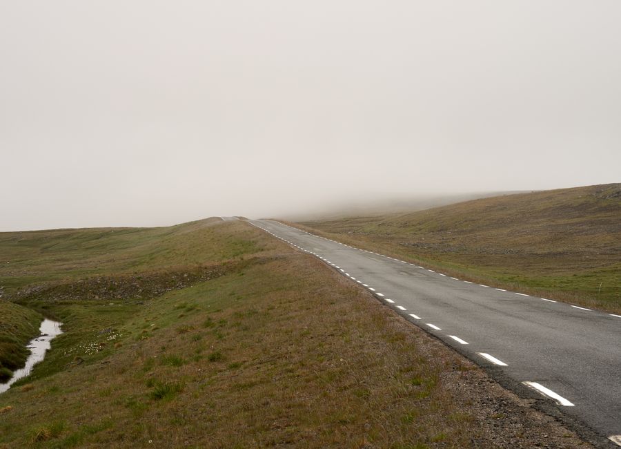 Lonely road in a foggy Norwegian landscape, creating a mysterious and serene atmosphere.