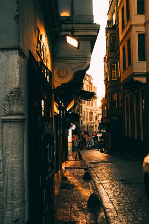 Free A picturesque cobblestone alleyway at sunset, illuminated by warm street lights in a historic city center. Stock Photo
