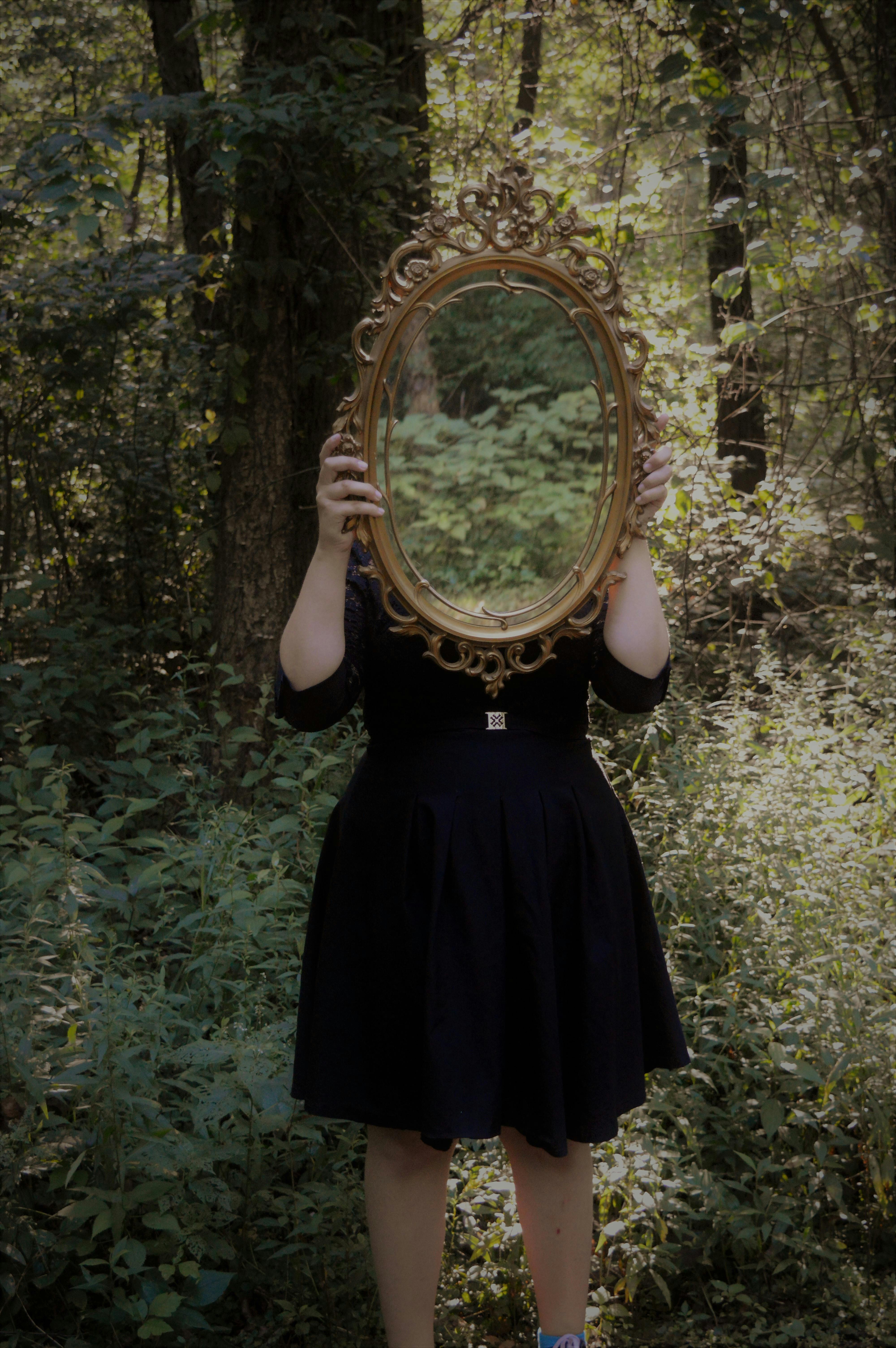 woman holding mirror against her head in the middle of forest