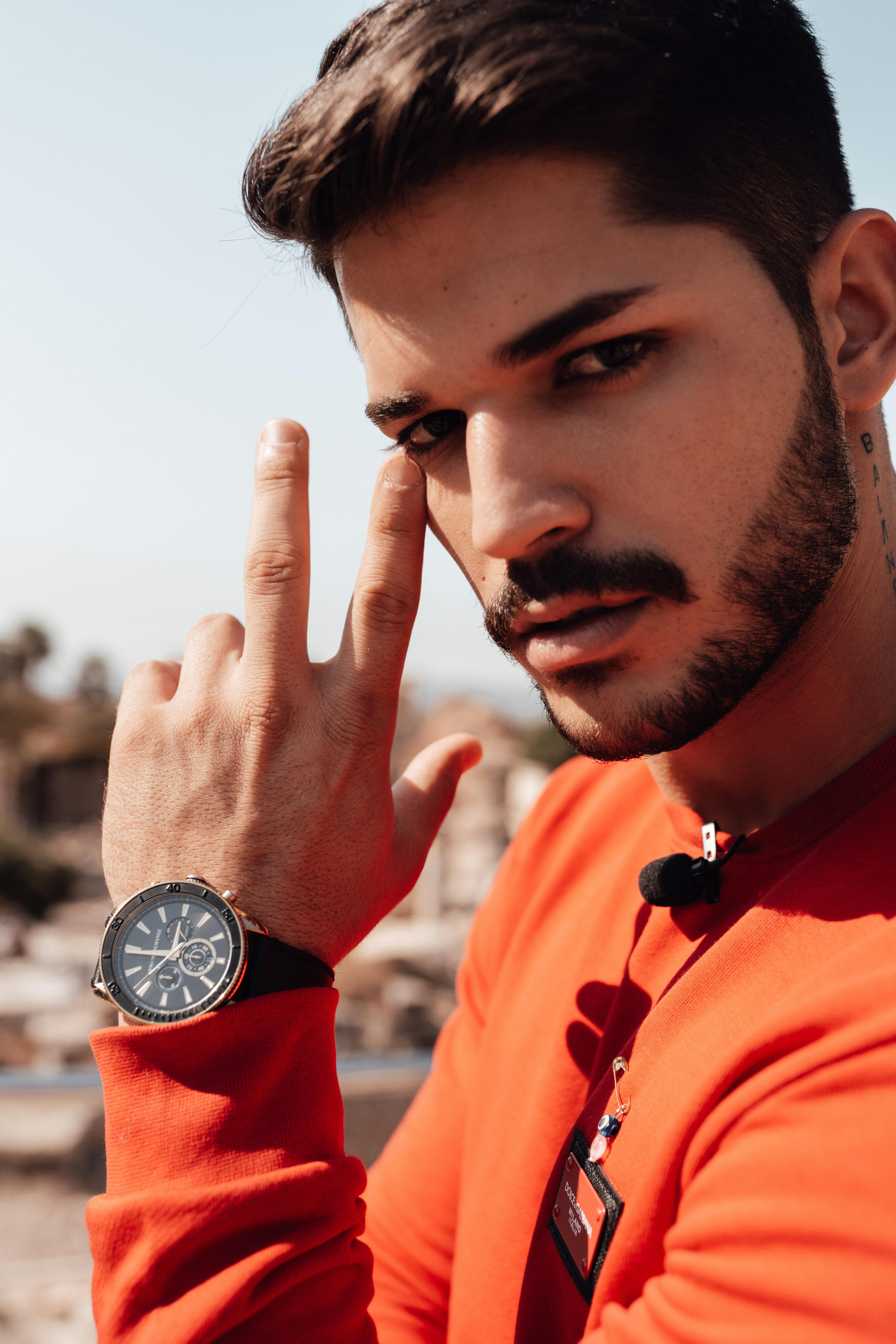 Fashionable young man with a beard wearing a wristwatch in a casual outdoor portrait.