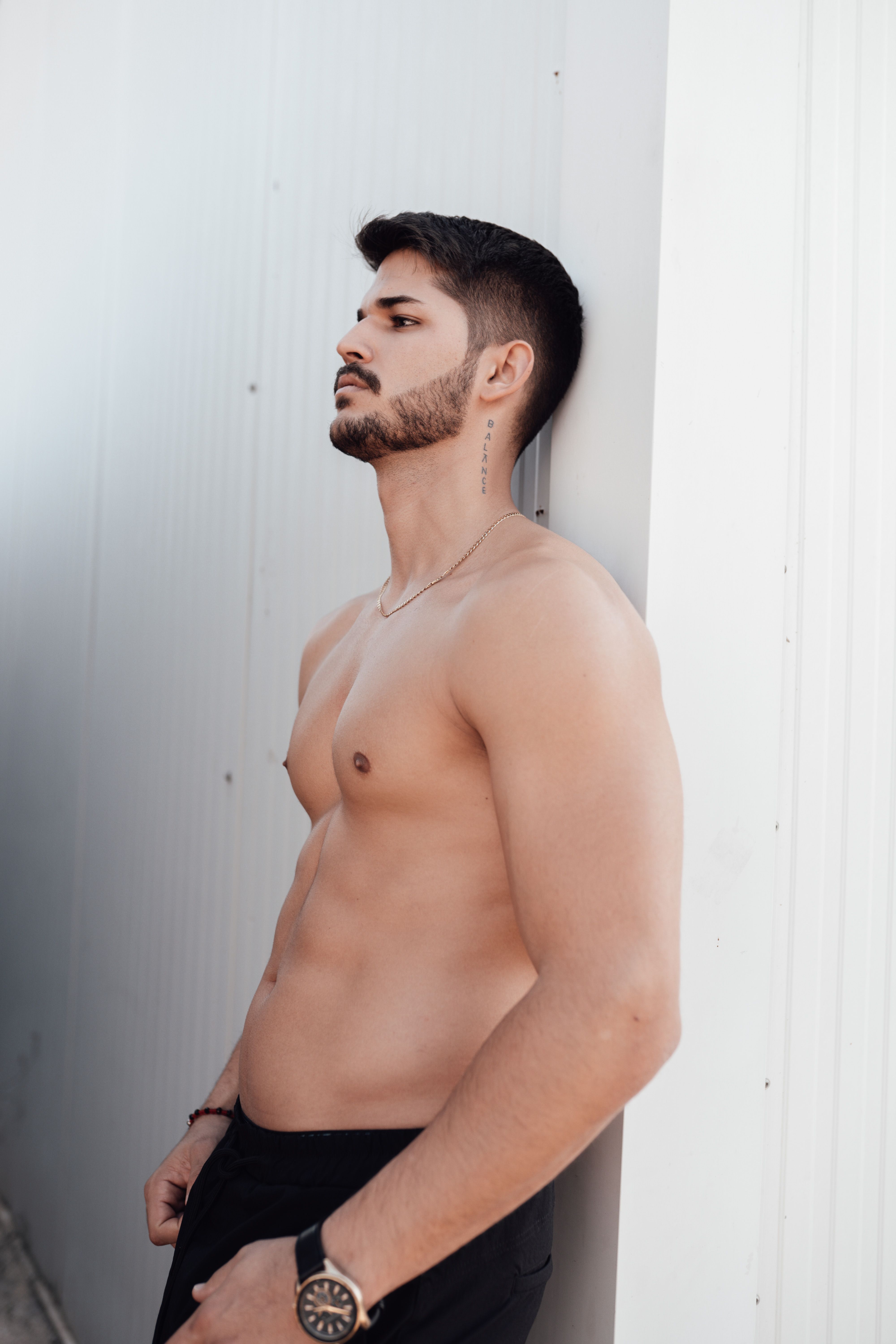 Stylish topless bearded man in profile pose next to a wall, exuding confidence and modernity.