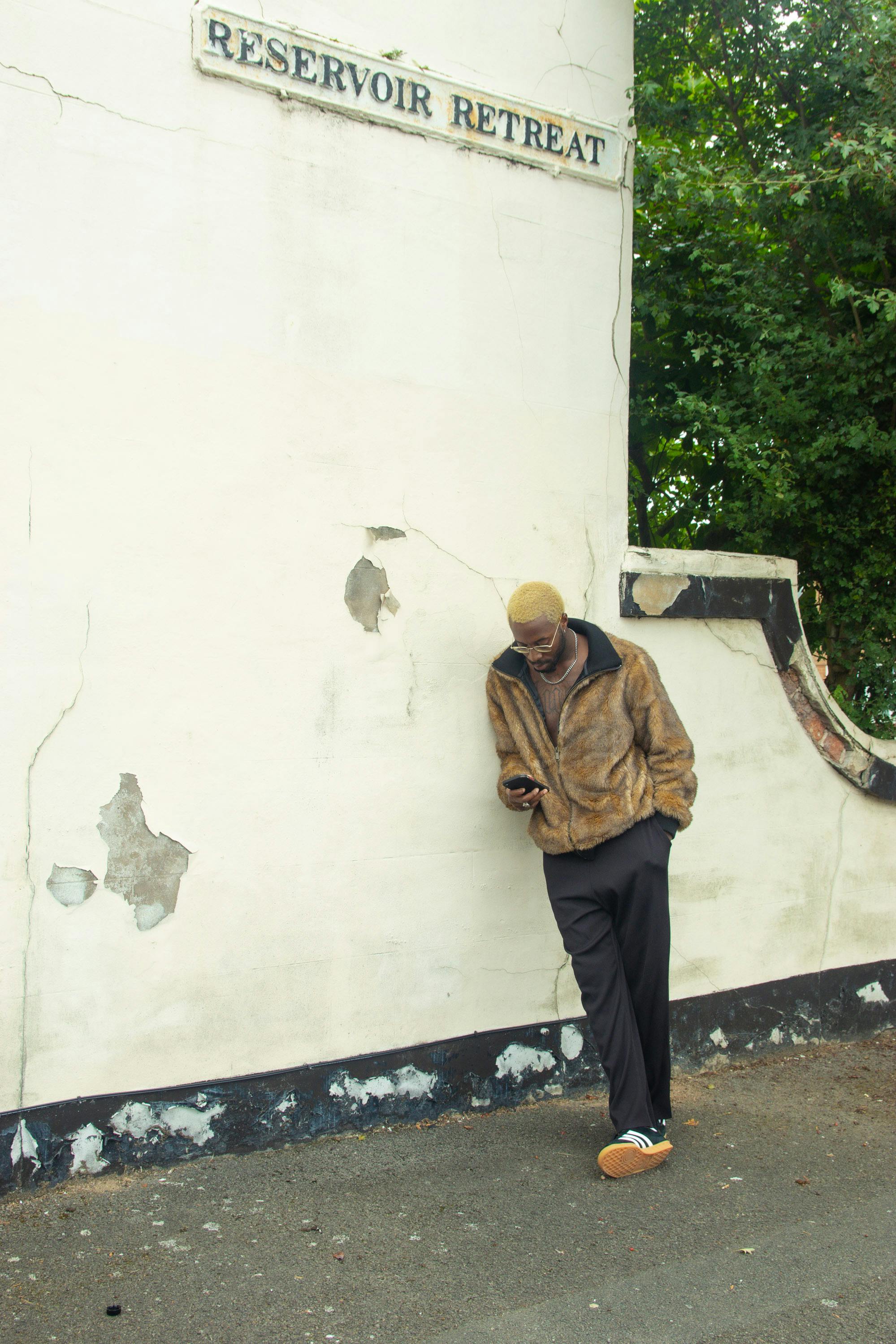 Stylish man using smartphone while leaning against a wall labeled 'Reservoir Retreat' in Birmingham, UK.