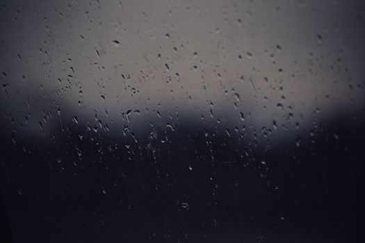 Artistic view of raindrops on a window during twilight, capturing a moody and serene atmosphere.
