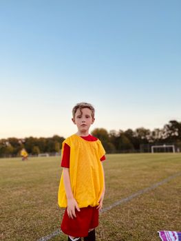 Young boy wearing sportswear standing on a soccer field during sunset.
