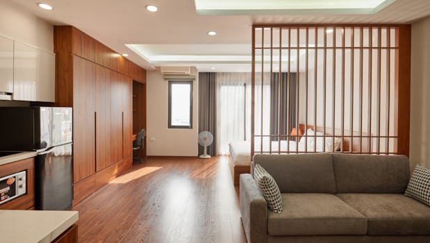 Spacious minimalist apartment with wooden accents, featuring sofa, bed, and ceiling lights in Hanoi.