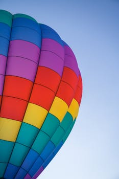Vibrant hot air balloon with rainbow stripes soaring in the clear blue sky.