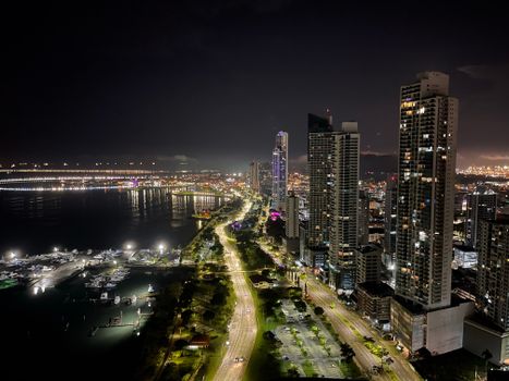 A breathtaking aerial view of a vibrant city at night, showcasing skyscrapers, roads, and a lit-up waterfront.