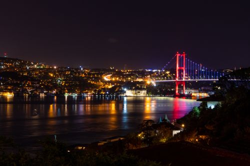 Free Stunning night view of the illuminated Bosphorus Bridge reflecting over the Bosphorus Strait in Istanbul. Stock Photo