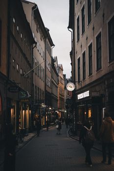 Discover the allure of a bustling urban alley with people strolling among historic buildings as evening descends.