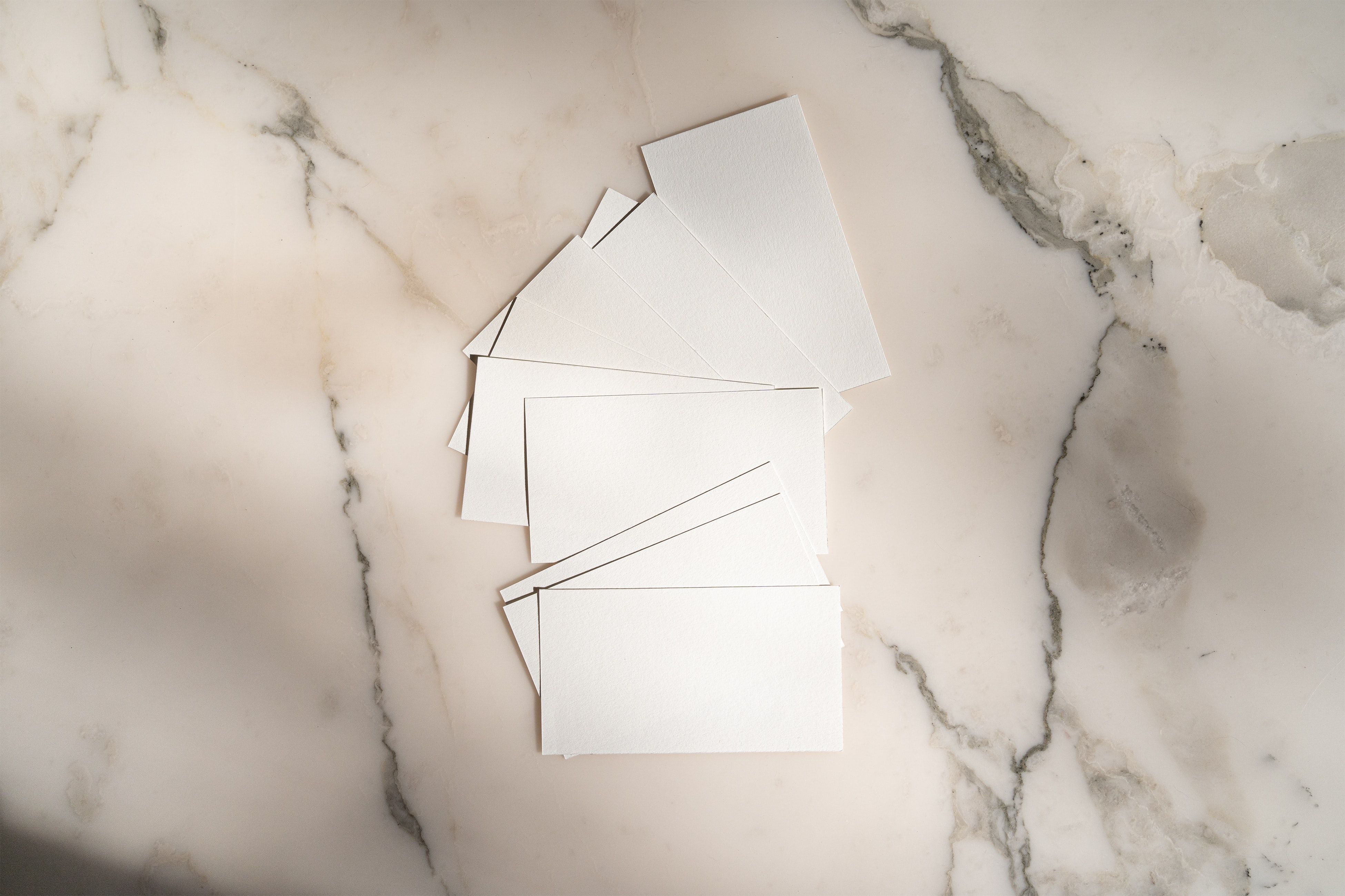 A flat lay of blank white cards arranged on a marble background for creative design use.