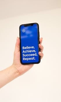 Close-up of a hand holding a smartphone with motivational text on the screen, emphasizing belief and success.
