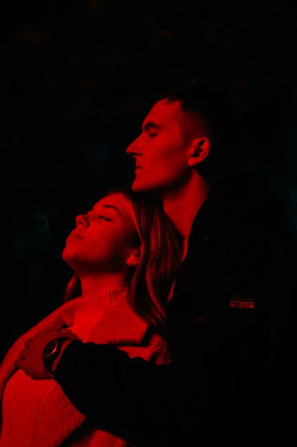 A couple embraces under moody red lighting, evoking intimacy and connection.