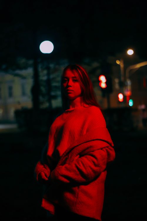 Free A woman stands under a red streetlight, conveying mystery and intrigue at night. Stock Photo