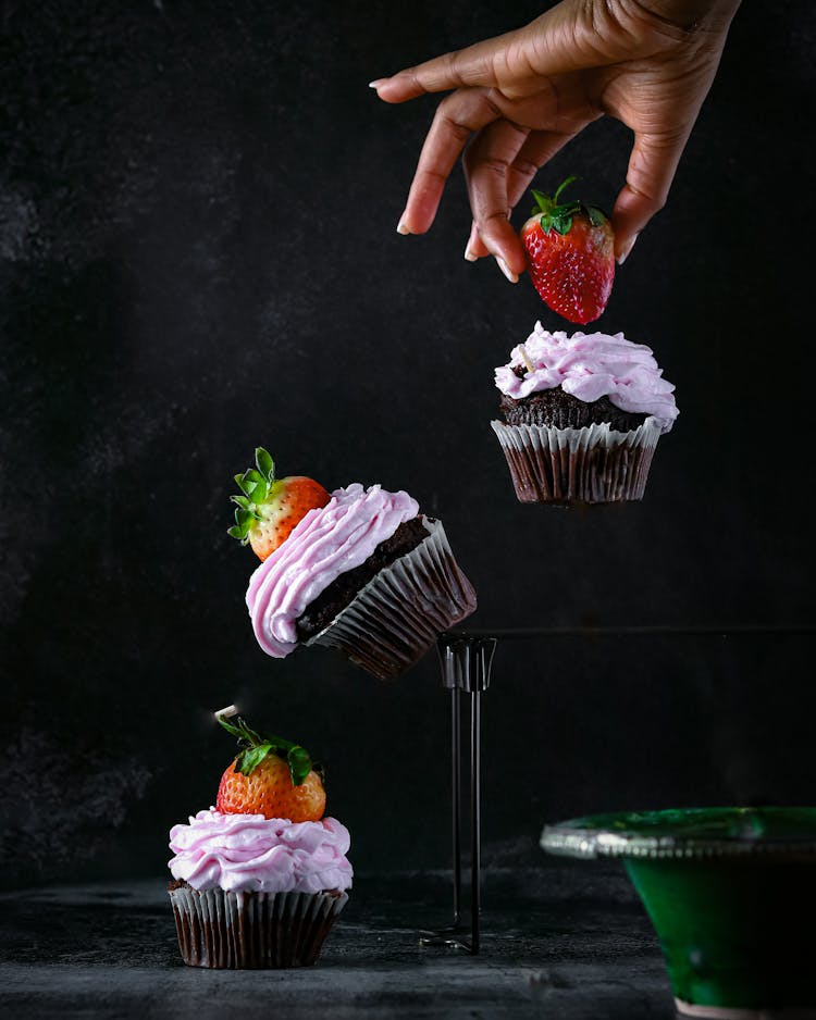 Human Hand Holding Strawberry On Cupcake