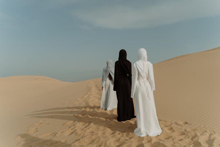 People Standing On The Sand While Wearing Long Dresses