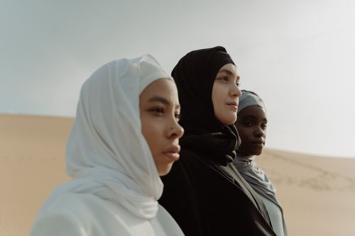 Free Three women in hijabs stand against a serene desert backdrop symbolizing unity and diversity. Stock Photo