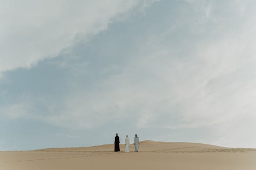 People standing on sand dunes under a vast sky, embracing cultural diversity.