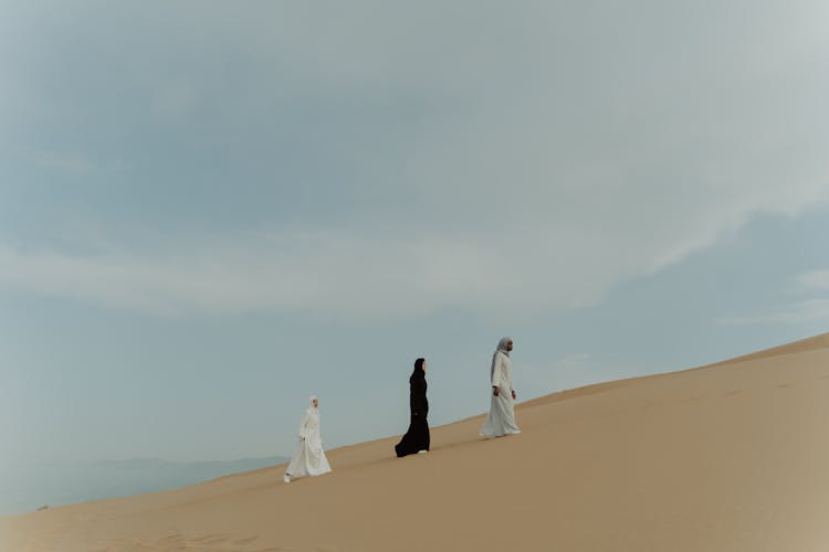 A Group Of People Walking In The Desert While Wearing Traditional Wear