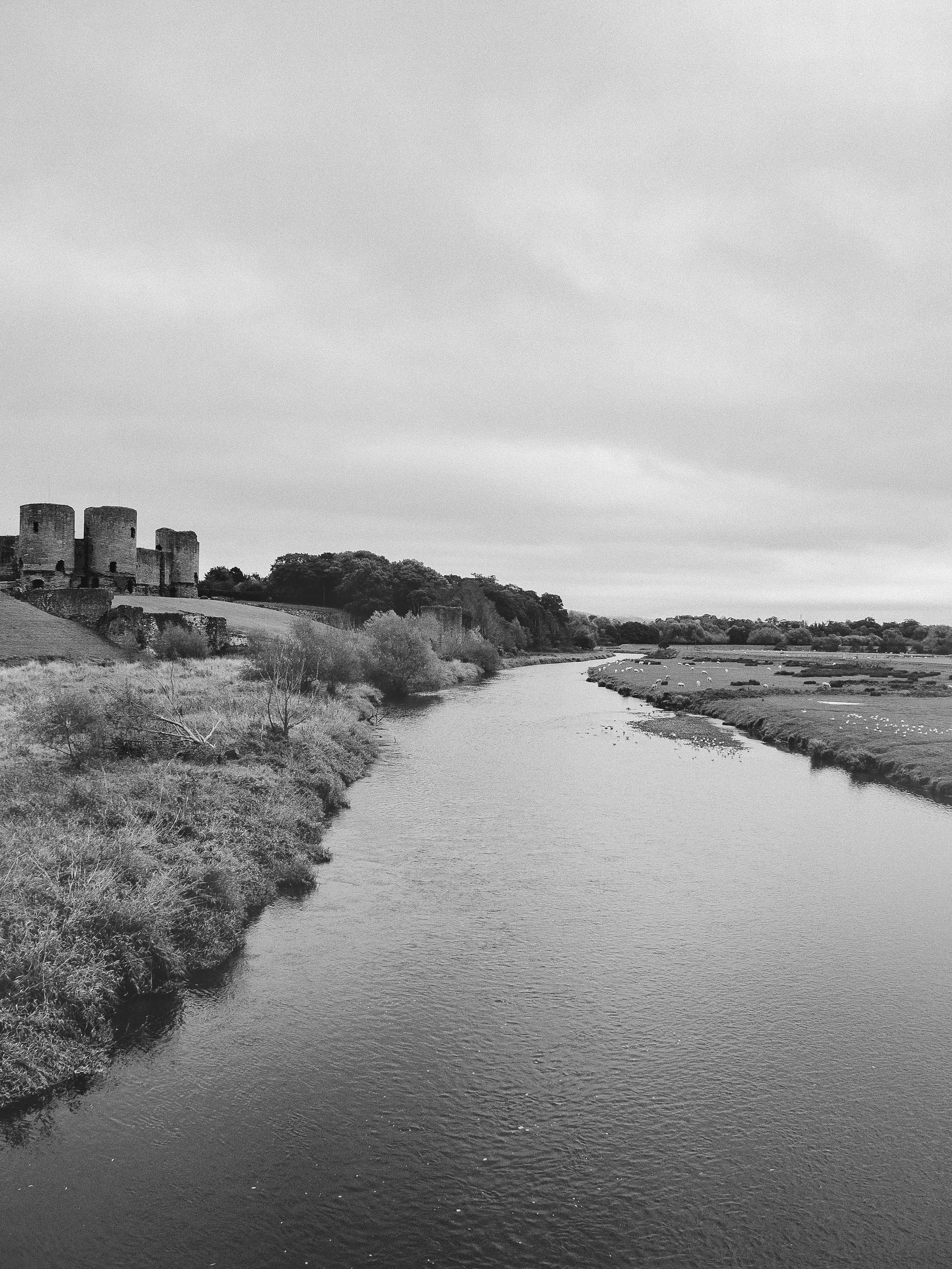 Monochrome view of a tranquil Welsh landscape featuring a historic castle by a river.