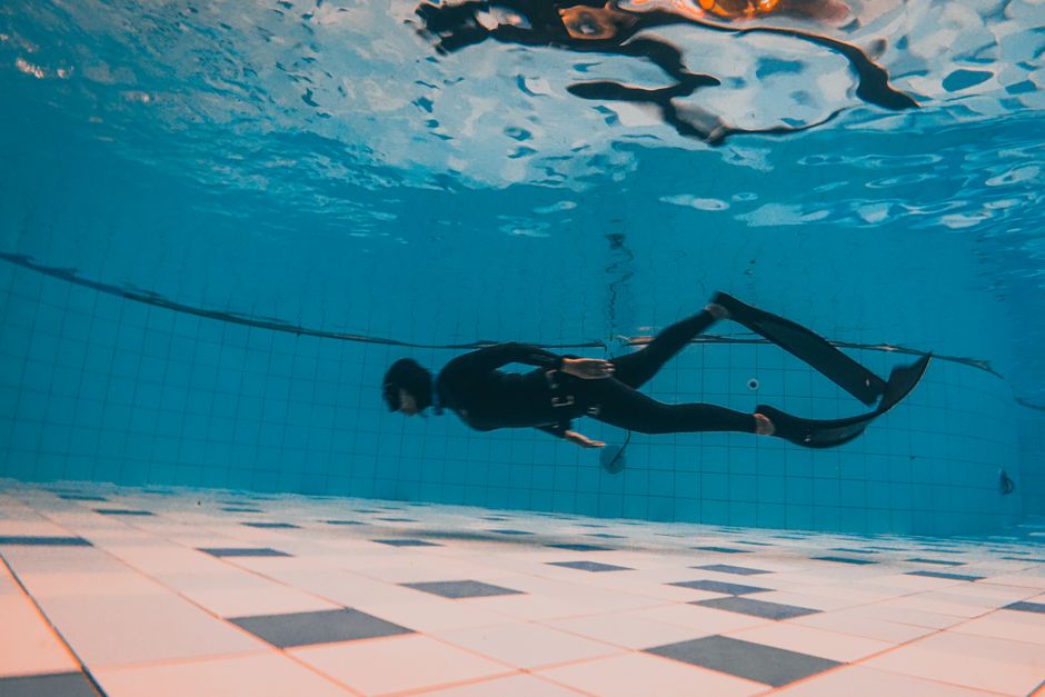 Diver gliding deep beneath a swimming pool, fins trailing with bubbles and shafts of light