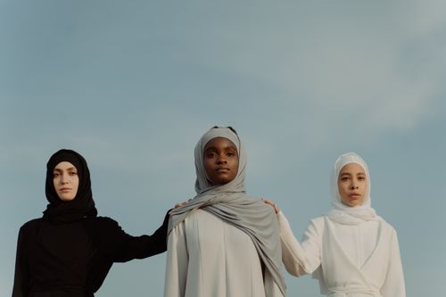 Free Three diverse women in hijabs stand united under a clear sky, symbolizing unity. Stock Photo