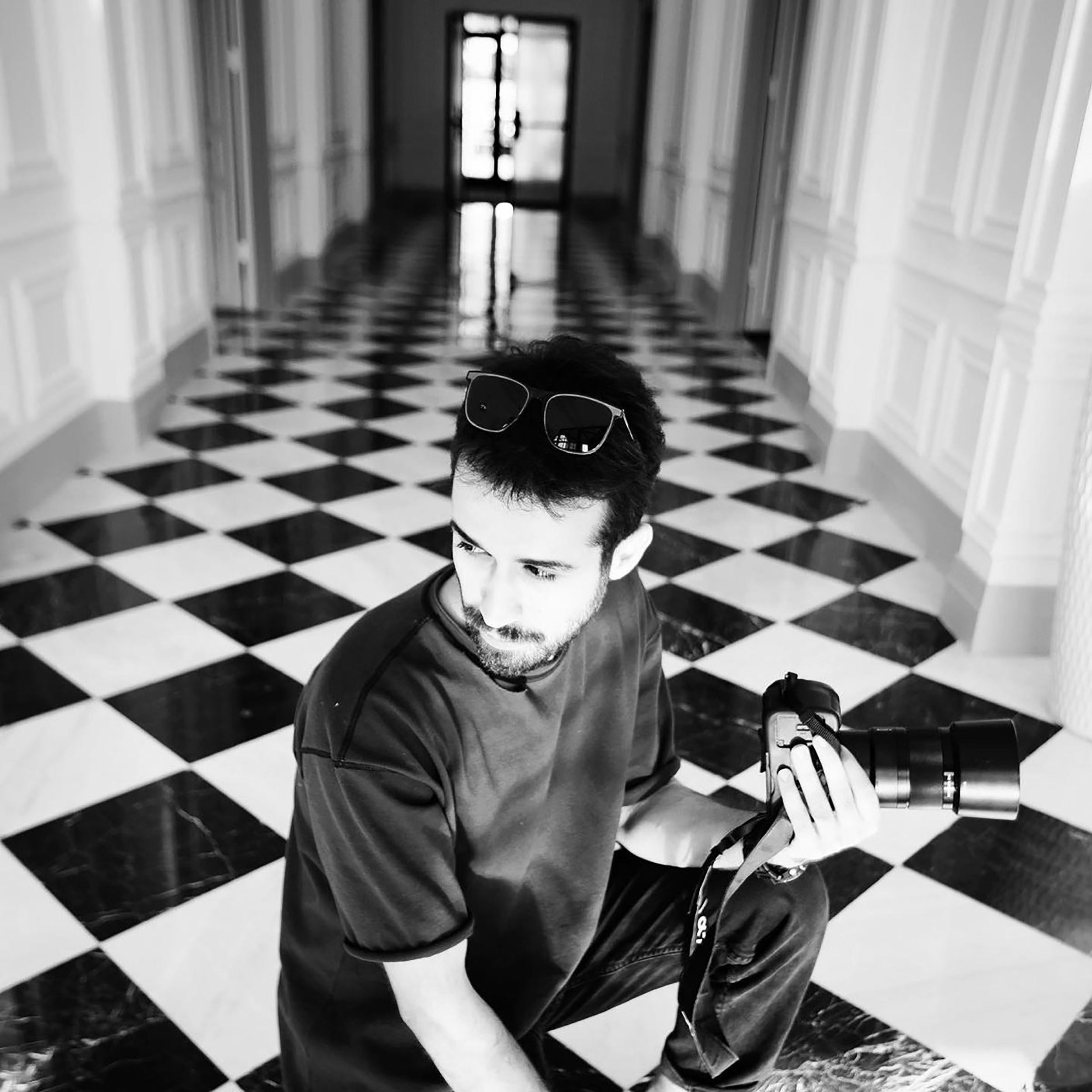Black and white portrait of a bearded photographer holding a camera indoors.