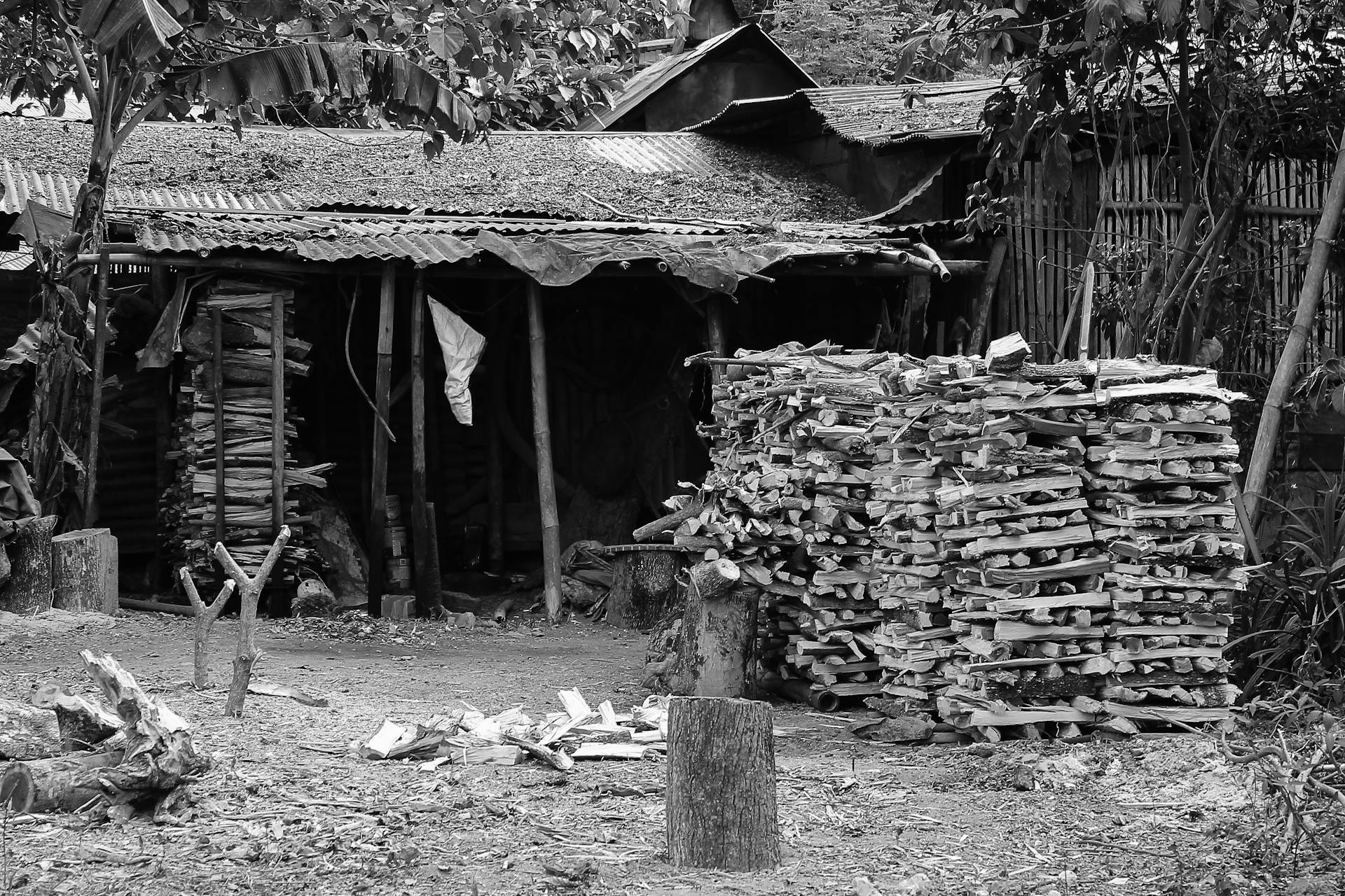 Black-and-white photo of stacked firewood by a rustic barn in a rural Philippine setting.