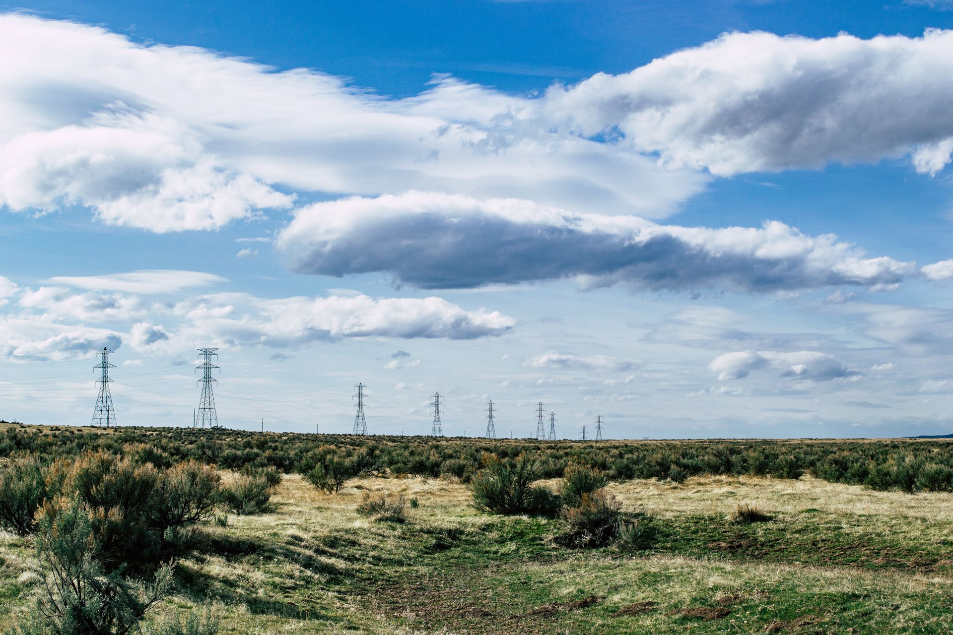 Expansive rural scene with power lines stretching across a countryside field under a vibrant blue sky.