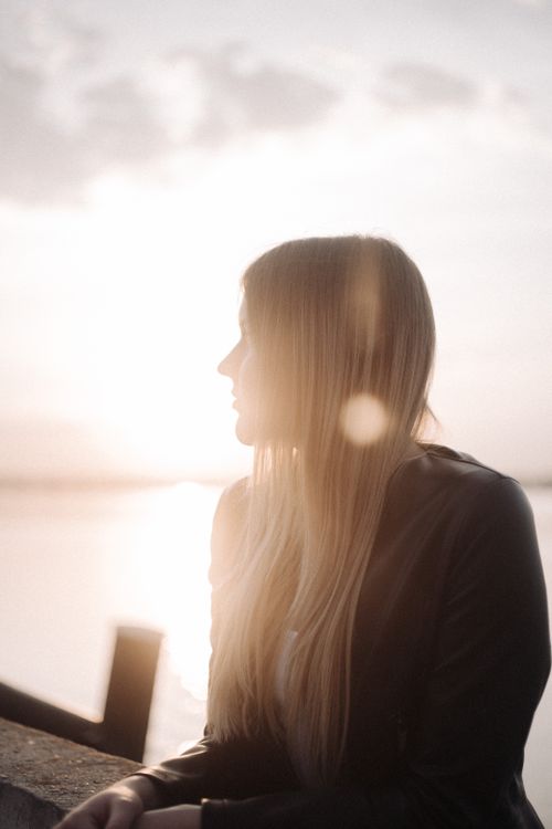 Free Silhouette of a woman with long hair gazing at a tranquil sunset over water. Stock Photo