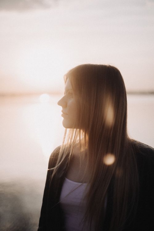 Free Profile of a young woman at sunset creating a tranquil mood by the water. Stock Photo