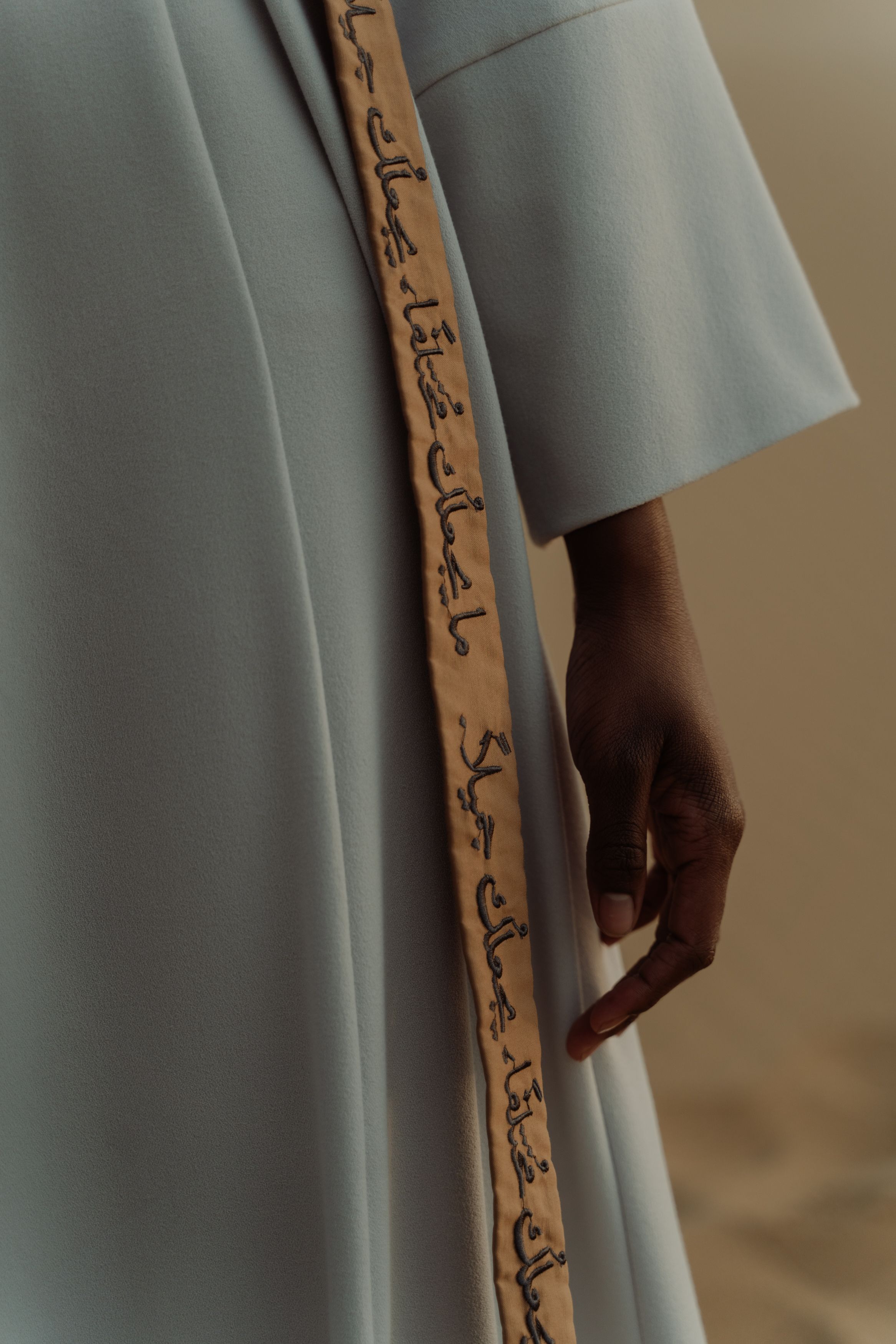 Close-up of a white dress with Arabic calligraphy details on the strap, showcasing elegant fashion design.