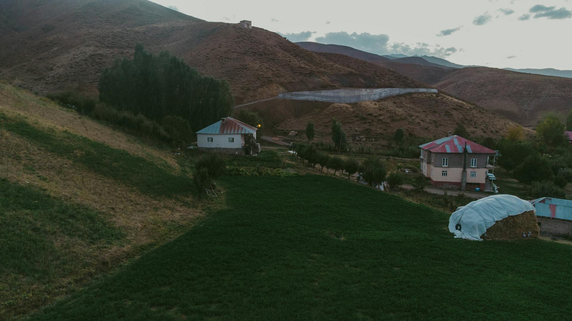 Scenic view of rural homes nestled in a hilly countryside at dusk, surrounded by fields and mountains.