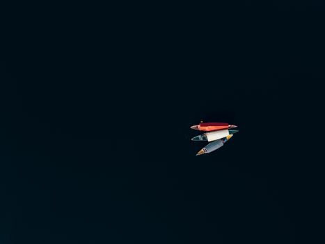 A minimalist aerial shot of three vibrant boats on calm, dark water, conveying tranquility.